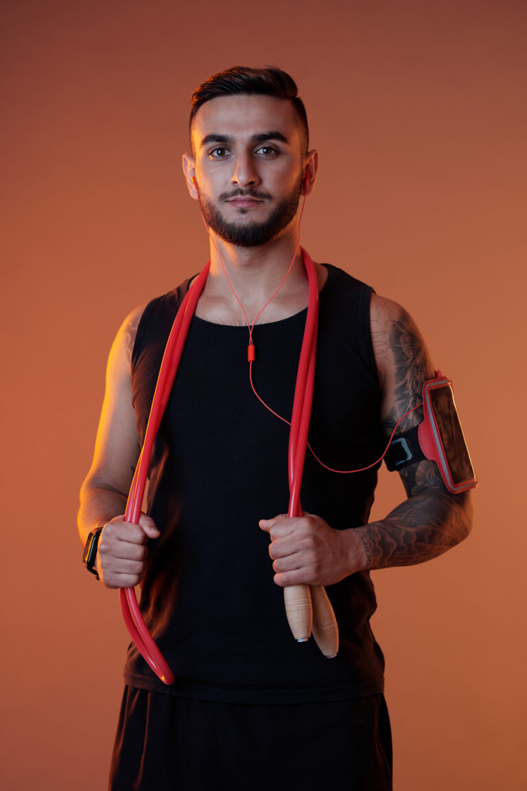 Handsome serious sportsman in headphones and armband holding jumping rope while looking at camera